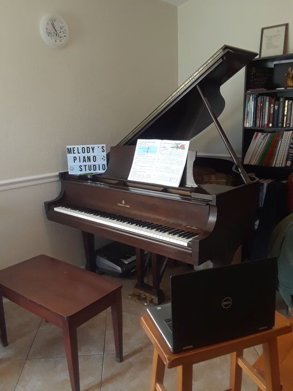 Steinway baby grand piano with computer on a stool nearby, set up for teaching online piano lessons