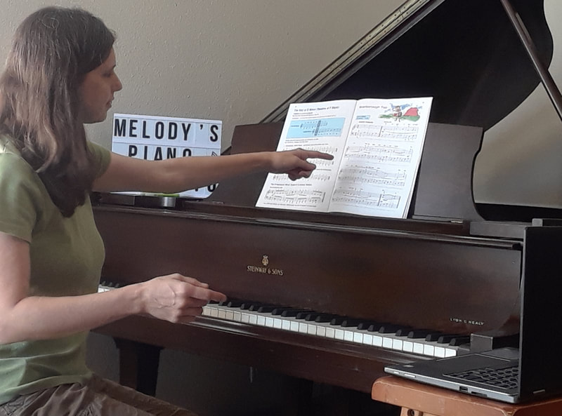 Teacher sitting at Steinway piano, pointing to music lesson book